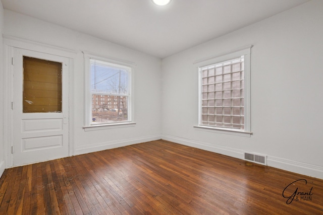 unfurnished room featuring dark wood-style floors, visible vents, and baseboards