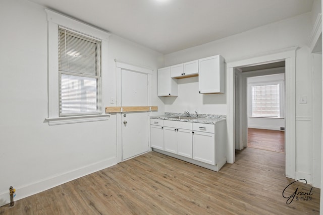 kitchen featuring light wood finished floors, white cabinets, baseboards, and a sink