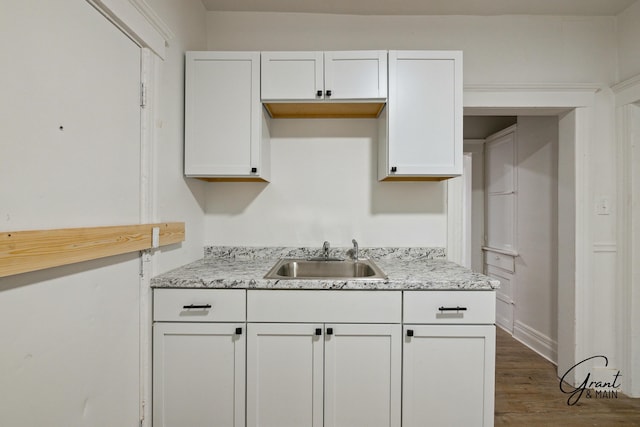 kitchen featuring dark wood-type flooring, white cabinets, light stone counters, and a sink