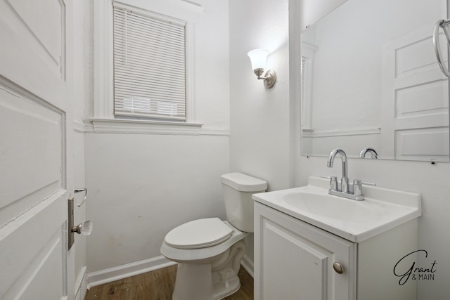 half bath with baseboards, toilet, wood finished floors, and vanity