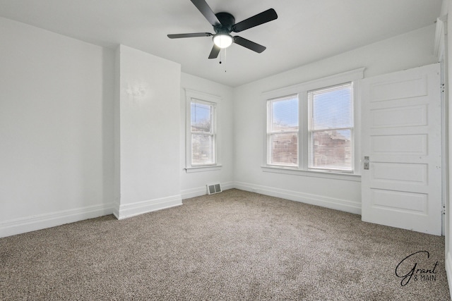 carpeted spare room featuring visible vents, a ceiling fan, and baseboards