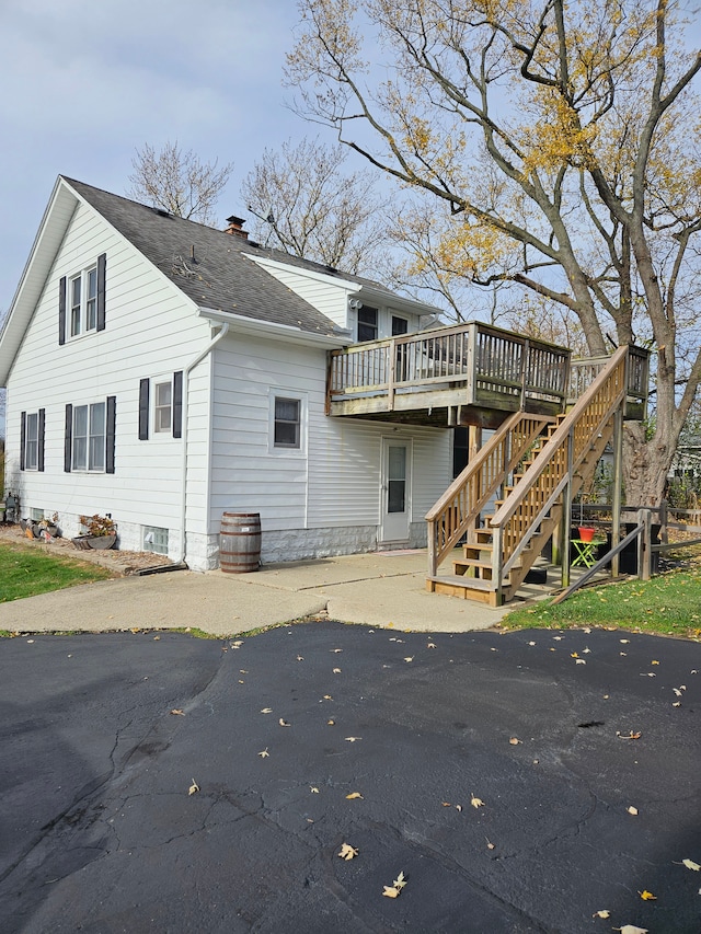 rear view of house with stairway, a wooden deck, a chimney, and a shingled roof