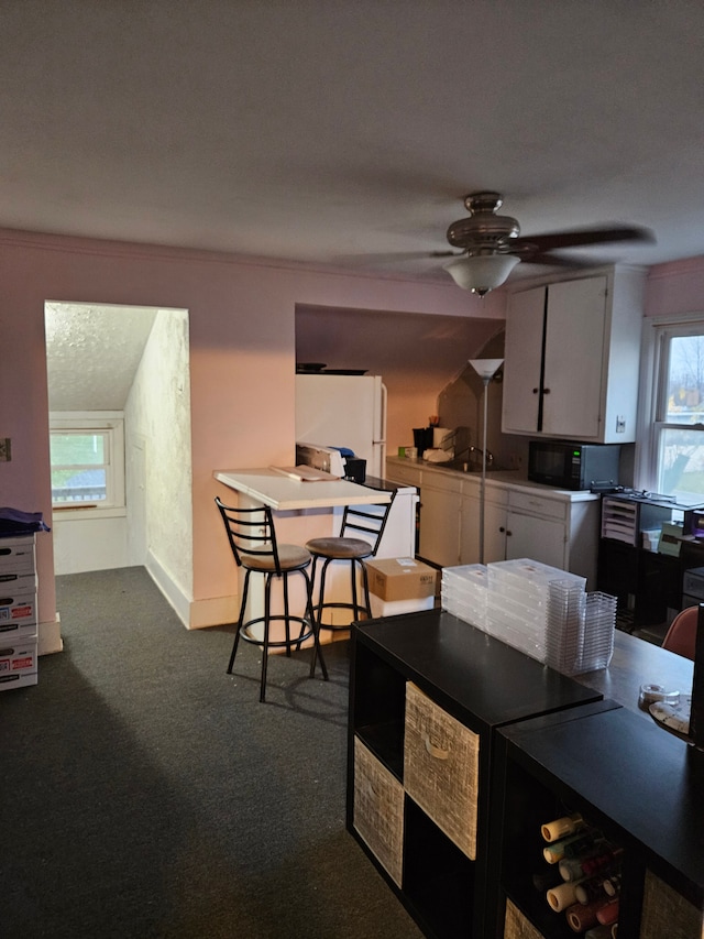 kitchen with dark carpet, white cabinetry, freestanding refrigerator, black microwave, and ceiling fan