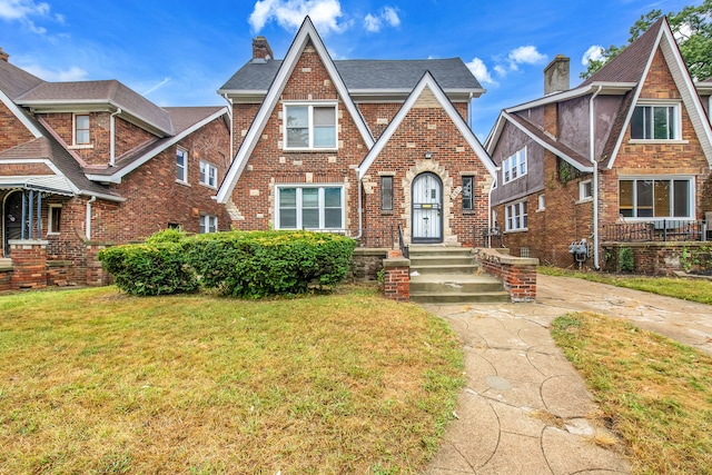 english style home with brick siding, a chimney, a shingled roof, and a front lawn