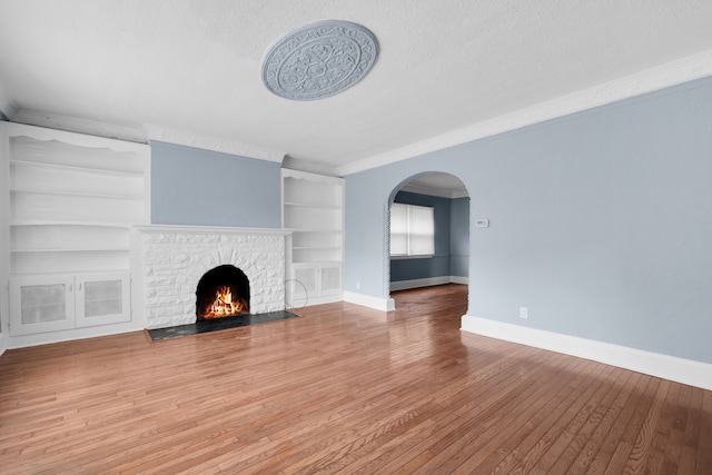 unfurnished living room featuring ornamental molding, hardwood / wood-style flooring, arched walkways, a fireplace, and baseboards