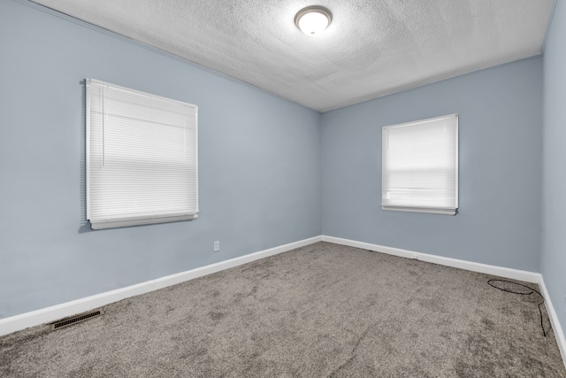 carpeted spare room with visible vents, baseboards, and a textured ceiling