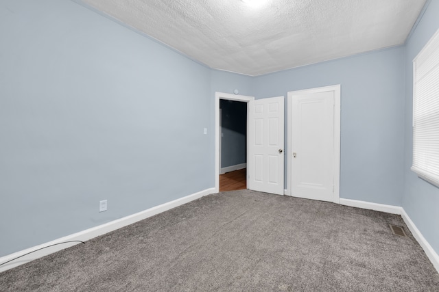 unfurnished bedroom featuring visible vents, multiple windows, a textured ceiling, carpet, and baseboards