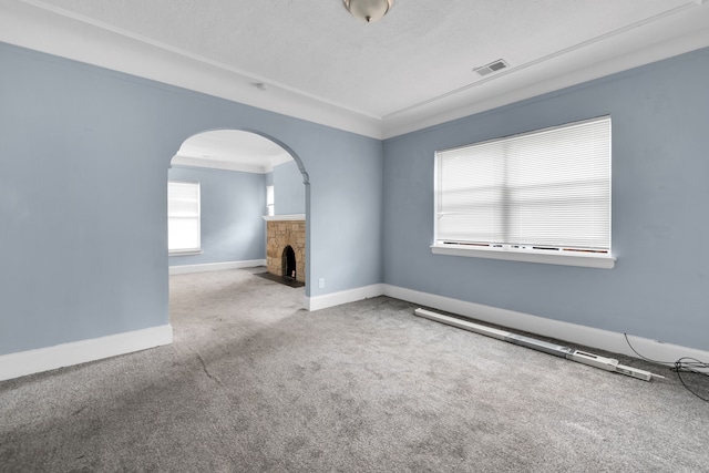 carpeted empty room with arched walkways, visible vents, baseboards, and a fireplace with flush hearth