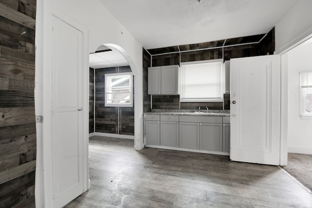 kitchen with a sink, wood-type flooring, arched walkways, and gray cabinetry