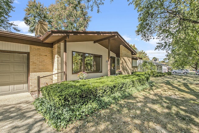 view of side of home featuring an attached garage, brick siding, and a chimney