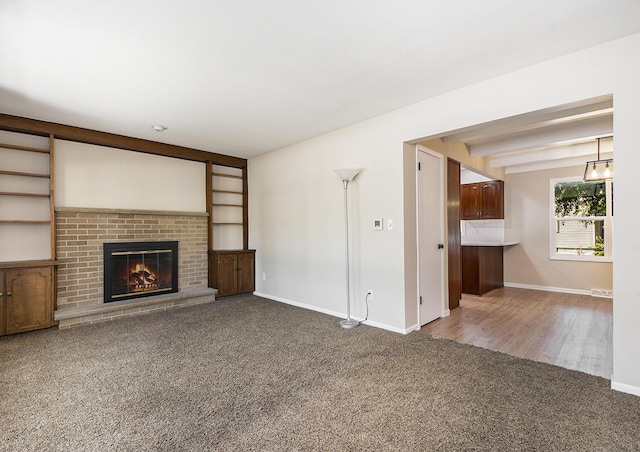 unfurnished living room with visible vents, baseboards, a fireplace, beamed ceiling, and carpet flooring