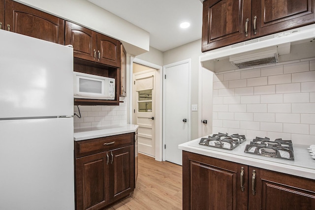 kitchen featuring white appliances, decorative backsplash, light countertops, light wood-style floors, and under cabinet range hood