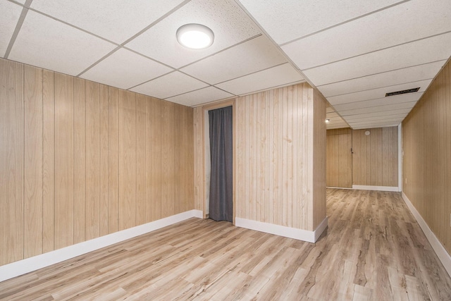 empty room featuring wooden walls, wood finished floors, and a paneled ceiling