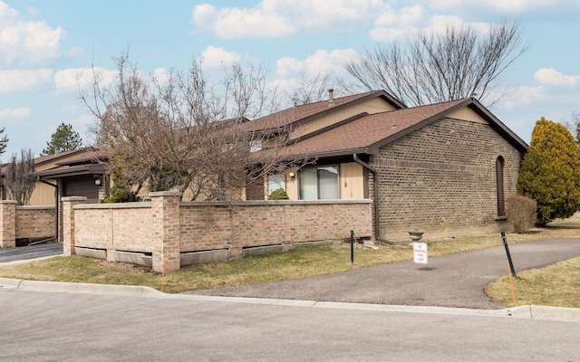 view of home's exterior with a fenced front yard, brick siding, roof with shingles, and a garage