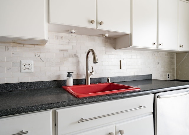 kitchen with a sink, dark countertops, white dishwasher, and white cabinetry