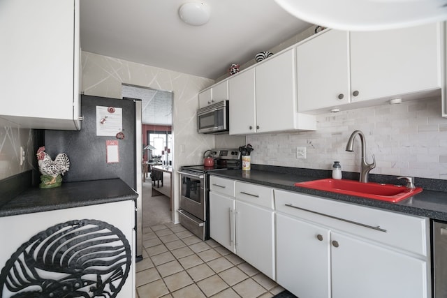 kitchen with dark countertops, tasteful backsplash, appliances with stainless steel finishes, white cabinetry, and a sink