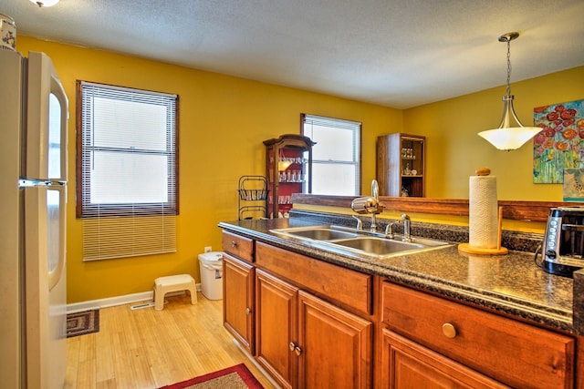 kitchen with pendant lighting, light wood-style flooring, a sink, dark countertops, and freestanding refrigerator