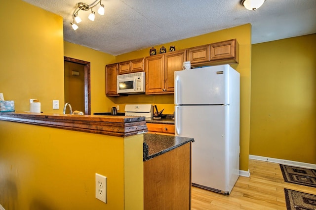 kitchen featuring light wood-style flooring, brown cabinetry, white appliances, a textured ceiling, and a sink