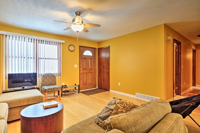 living area with visible vents, light wood finished floors, and a textured ceiling