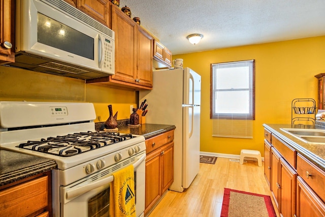 kitchen featuring light wood-type flooring, brown cabinets, a sink, a textured ceiling, and white appliances