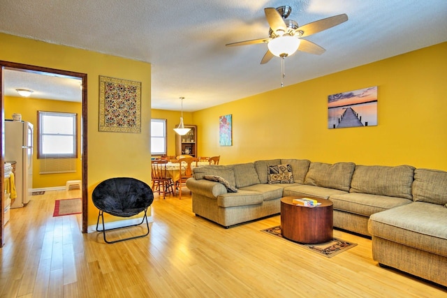 living room with light wood-type flooring, baseboards, a textured ceiling, and a ceiling fan