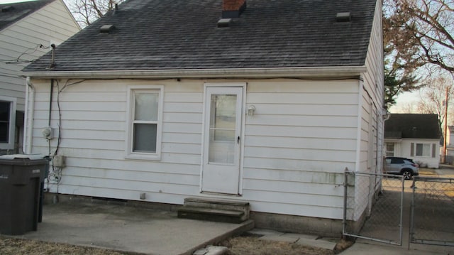 back of house featuring entry steps, a chimney, roof with shingles, and fence