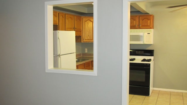 kitchen with white appliances, light tile patterned floors, a ceiling fan, baseboards, and brown cabinets