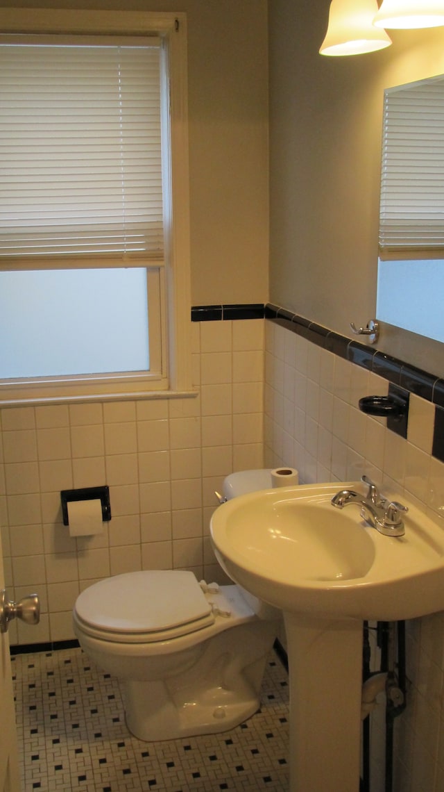 half bathroom with tile patterned floors, toilet, and tile walls