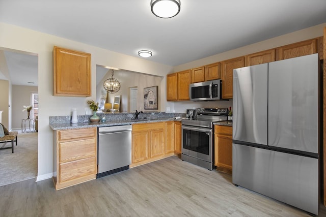 kitchen featuring stone counters, a sink, appliances with stainless steel finishes, light wood-type flooring, and a chandelier