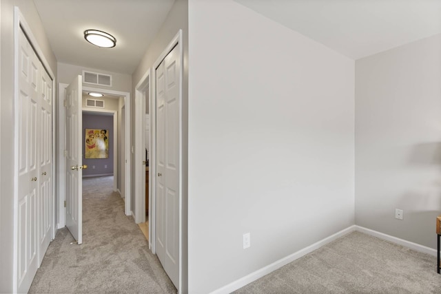 hallway featuring light colored carpet, visible vents, and baseboards