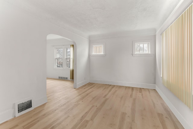 empty room featuring arched walkways, visible vents, a textured ceiling, and light wood-type flooring