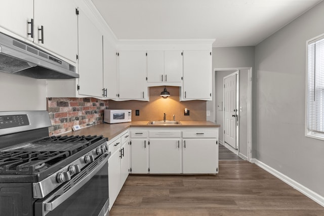 kitchen featuring white microwave, stainless steel range with gas cooktop, under cabinet range hood, decorative backsplash, and a sink