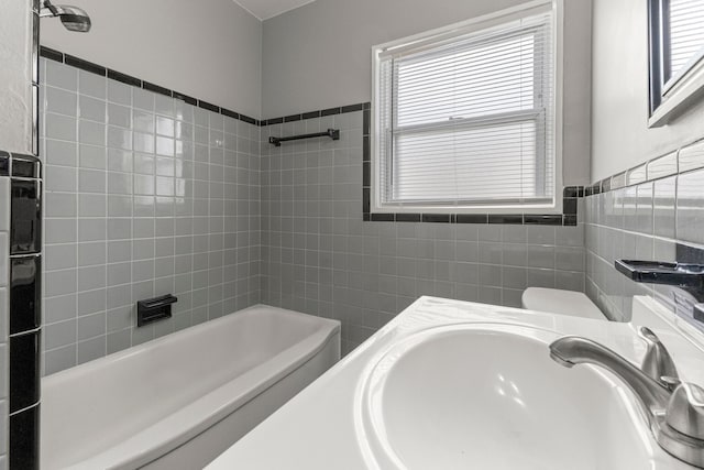 bathroom with toilet, tile walls, shower / bath combination, and a sink