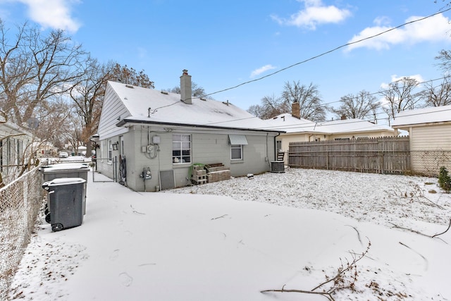 snow covered property featuring cooling unit, a chimney, and fence