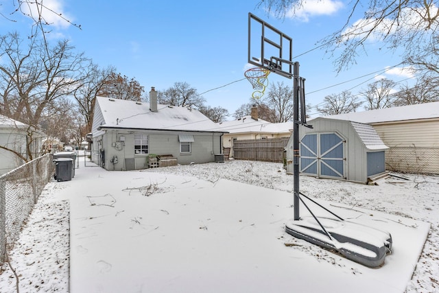 snow covered house with an outbuilding, a storage unit, fence, and a chimney