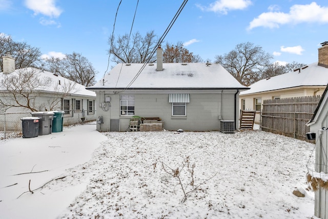 snow covered back of property featuring central AC unit, fence, and a chimney