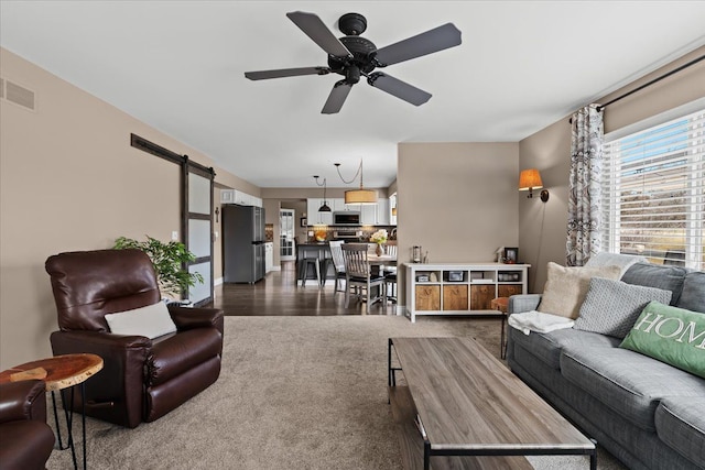 living area featuring visible vents, a barn door, ceiling fan, and dark carpet