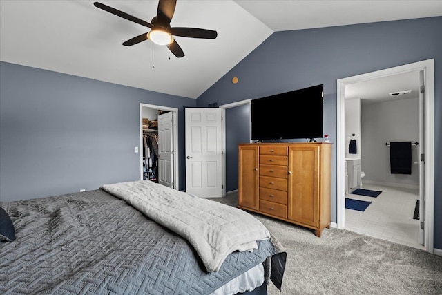 bedroom featuring ceiling fan, vaulted ceiling, light carpet, a walk in closet, and connected bathroom