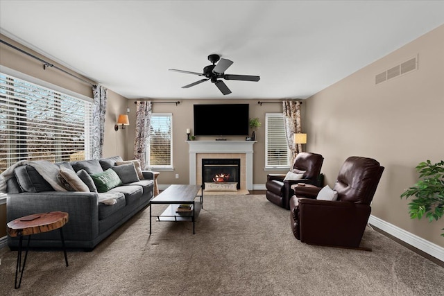 living area with visible vents, baseboards, a tiled fireplace, carpet flooring, and a ceiling fan