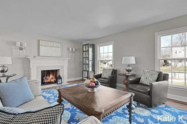 living area featuring visible vents, a fireplace with flush hearth, baseboards, and wood finished floors