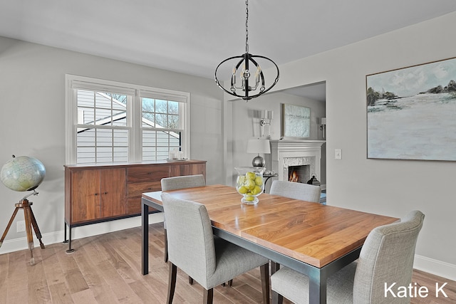 dining room with a high end fireplace, light wood-style flooring, baseboards, and an inviting chandelier