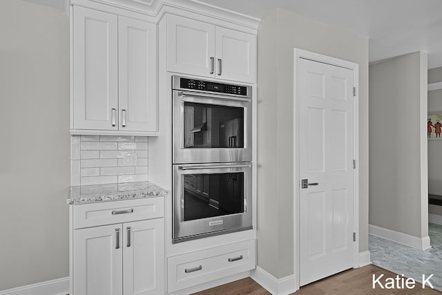 kitchen with backsplash, light stone countertops, wood finished floors, stainless steel double oven, and white cabinets