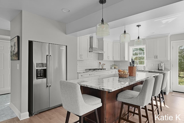 kitchen with white cabinetry, wall chimney range hood, light wood finished floors, and appliances with stainless steel finishes