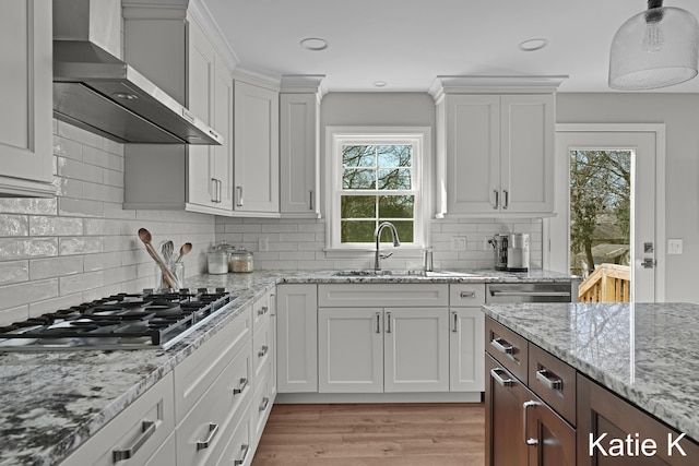 kitchen with light wood-type flooring, a sink, stainless steel gas stovetop, white cabinets, and wall chimney range hood