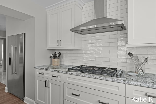 kitchen featuring dark wood-style flooring, stainless steel appliances, decorative backsplash, white cabinetry, and wall chimney exhaust hood