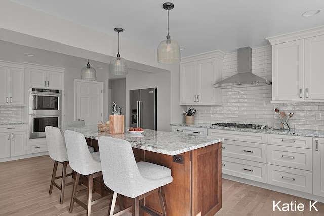 kitchen with appliances with stainless steel finishes, wall chimney exhaust hood, white cabinets, and light wood finished floors