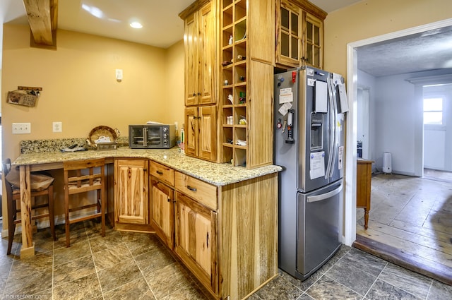 kitchen featuring light stone counters, baseboards, stone finish floor, glass insert cabinets, and stainless steel fridge