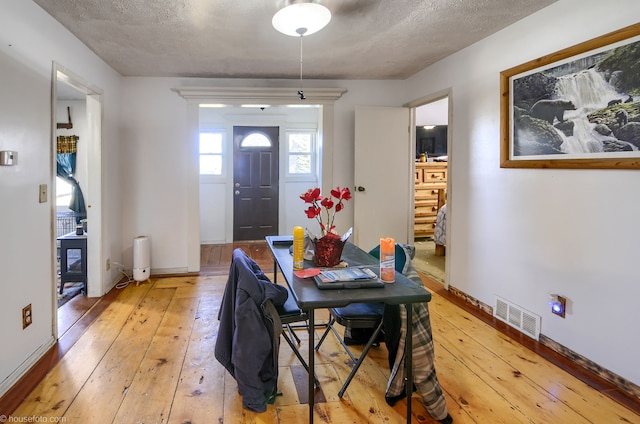 dining area with a textured ceiling, baseboards, visible vents, and light wood-type flooring