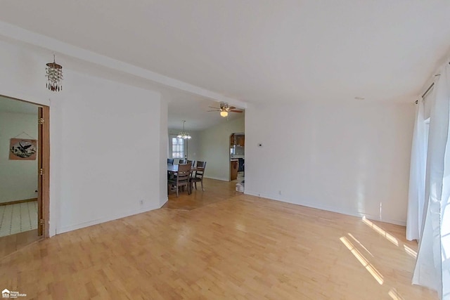 unfurnished room featuring lofted ceiling, light wood-style flooring, ceiling fan with notable chandelier, and baseboards