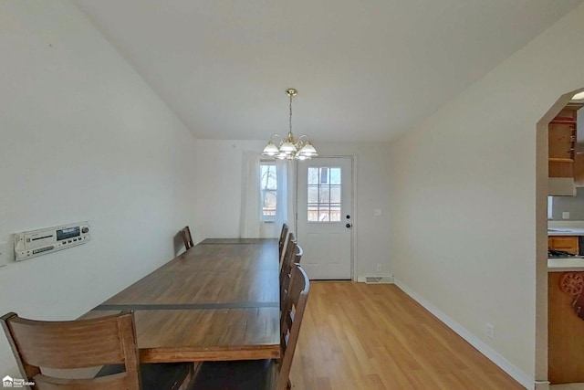 dining room with arched walkways, an inviting chandelier, light wood finished floors, baseboards, and vaulted ceiling